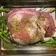 Raw pork shoulder rubbed with fennel seeds on top of fennel, garlic, and onions in a roasting pan